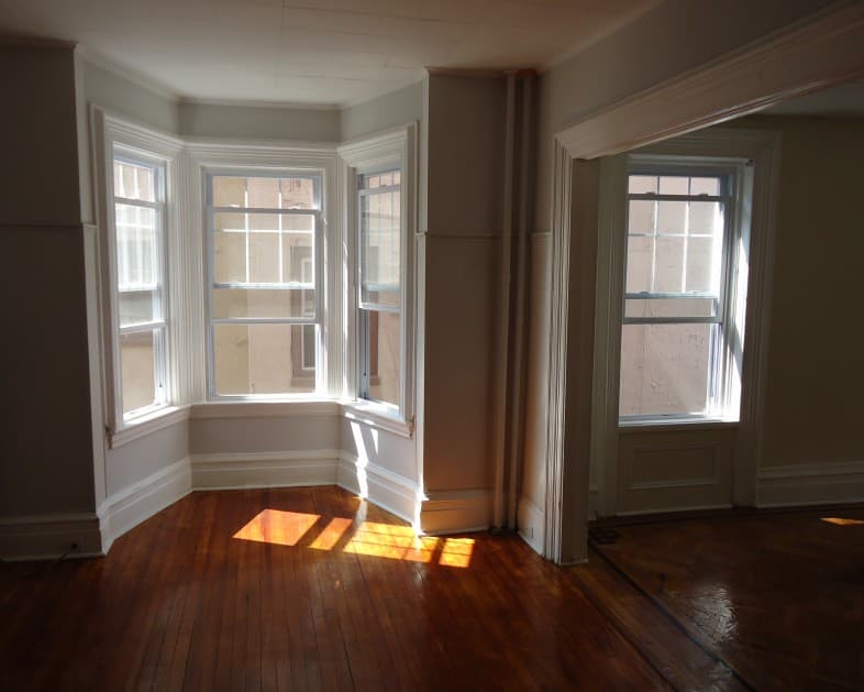 Empty room with polished hardwood floors and a sunlit bay window